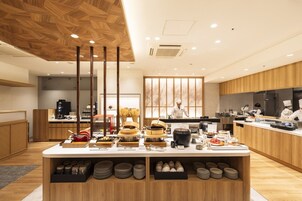 Un restaurante moderno con una mesa de buffet central, zona de cocina y techo de madera.