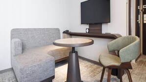 A modern room with a grey sofa, a round wooden table, and a green armchair. A flat-screen TV is mounted on the wall above the table.