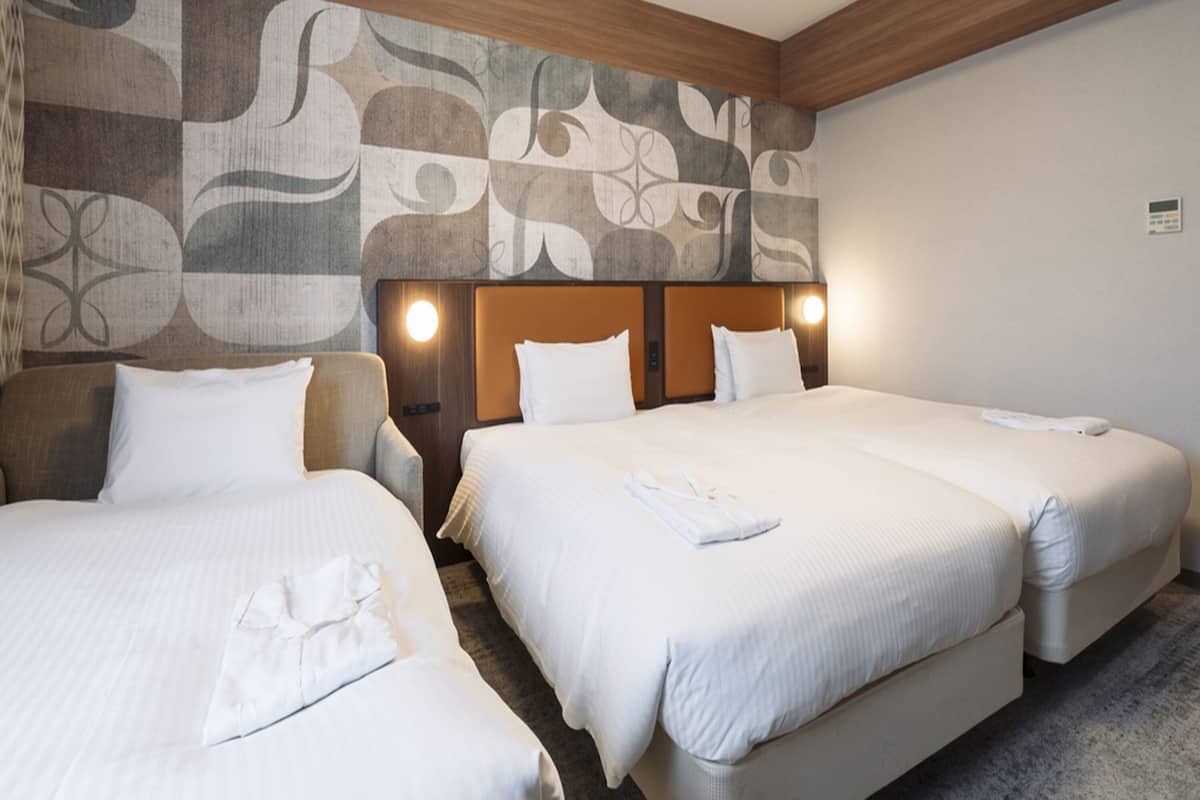 A hotel room with three beds, a wooden headboard, and a patterned wall.