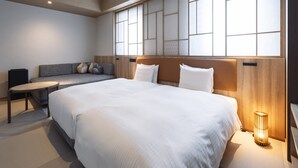A modern hotel room with a large bed, a sofa, a small table, and a large window with a view.
