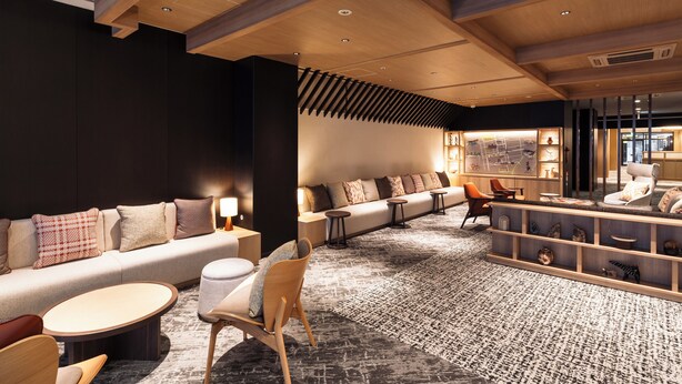 A modern hotel lobby with a sofa, chairs, a coffee table, and a reception desk.