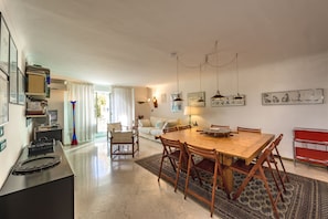 Uma sala espaçosa com uma mesa de jantar de madeira, cadeiras, um sofá e uma estante de metal vermelha.