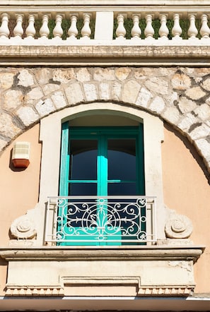 Fachada de edifício com arco de pedra, porta verde-água e varanda com grades de metal ornamentadas.