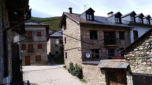A narrow stone street with traditional stone buildings, some with wooden shutters and balconies.