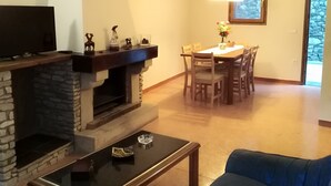 A living room with a stone fireplace, a television, a dining area with a table and chairs, and a blue sofa.