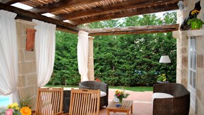 An outdoor patio area with wicker furniture, a table with a vase of flowers, and a view of a lush garden. - Rock House's Villa Rhapsody  (2 Bedrooms, Sleeps 4) with private garden and pool (Crete)