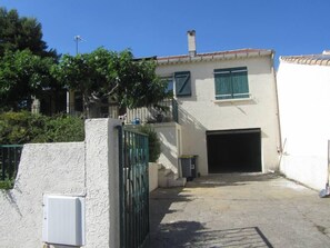 Un immeuble avec un garage, une entrée sécurisée par un portail et un petit arbre devant.