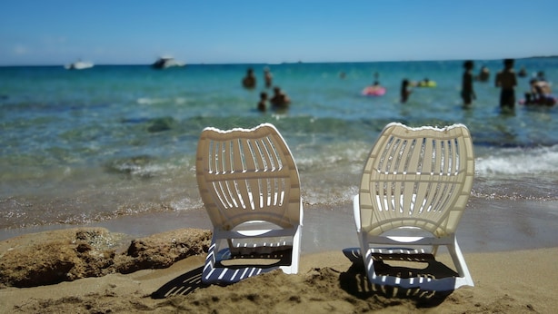 Dos sillas de playa mirando al océano, con gente nadando al fondo.