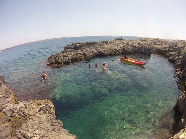 A rocky coastal area with clear water, a red kayak, and people swimming.