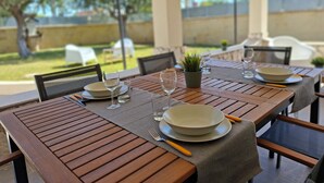 Mesa de madera preparada para comer al aire libre, con vista a un jardín y cielo despejado.