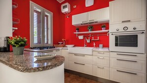 Una cocina con armarios blancos, encimera de granito y pared roja.