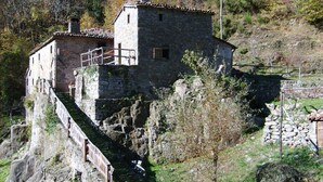 A stone building with a staircase leading up to it, surrounded by trees and rocky terrain. - Ancient mill in the "green hearth" of Tuscany (Pieve Fosciana)
