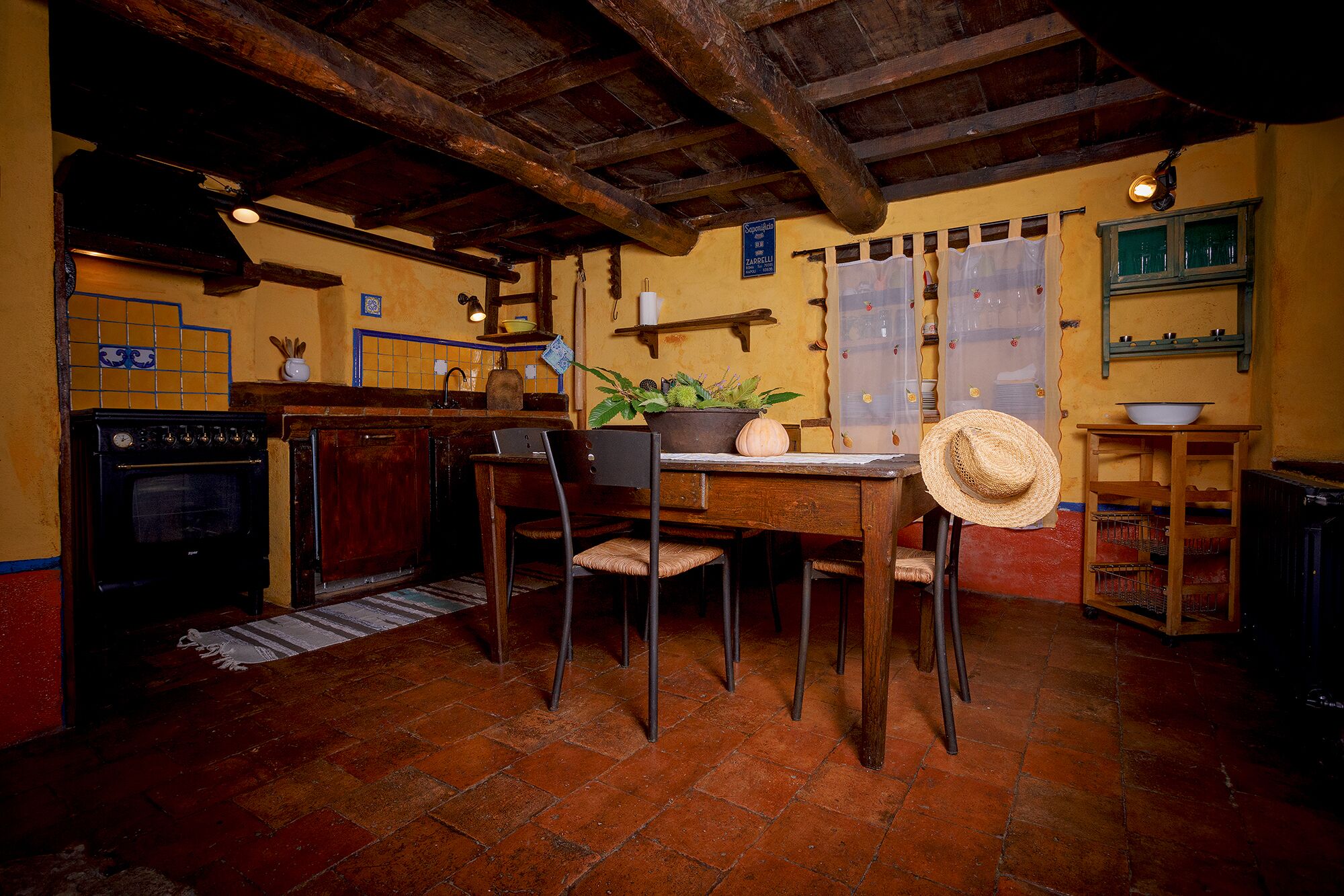 A rustic kitchen with exposed wooden beams, a stove, and a dining area with chairs and a table.