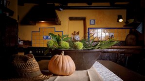 A rustic kitchen with a wooden table, a woven basket, a pumpkin, and a potted plant with green foliage and purple flowers. - Ancient mill in the "green hearth" of Tuscany (Pieve Fosciana)