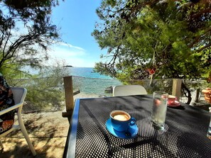 A table with a blue cup and a glass of water, overlooking a coastal view with trees and a clear sky. - Seaview Apts, 80 meters to beach, crystal clear sea, 2 apts, large terraces, BBQ (Rogoznica)