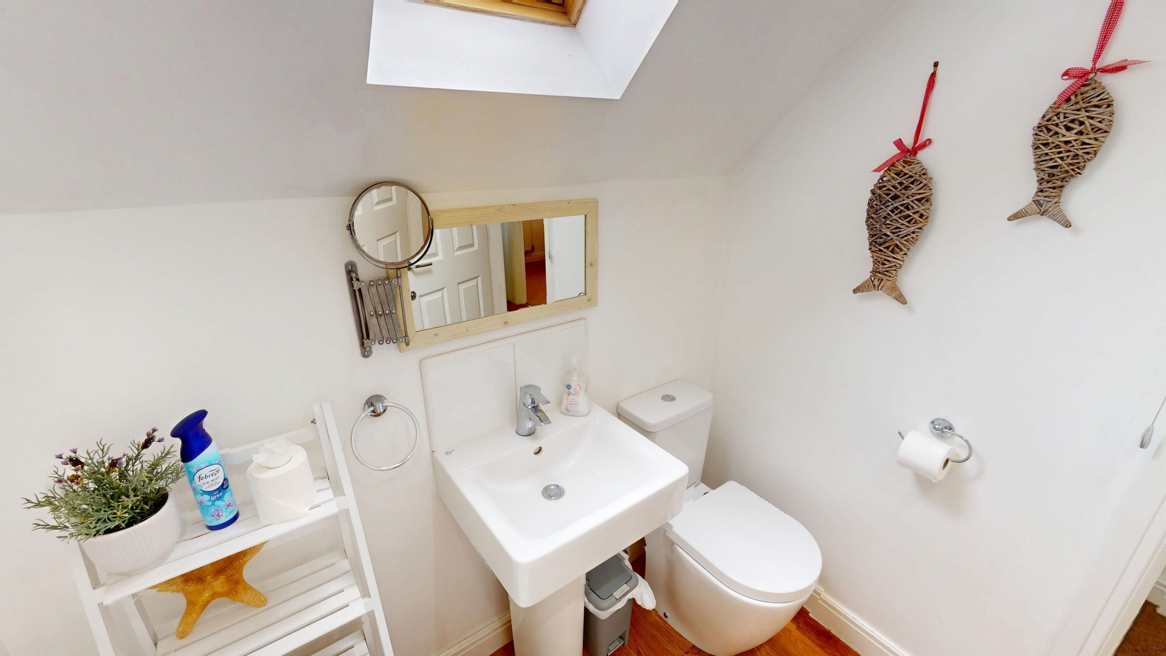Un bany amb un vàter, un lavabo i un mirall sobre el lavabo. Hi ha dos peixos decoratius a la paret i una estrella de mar a l'estant.