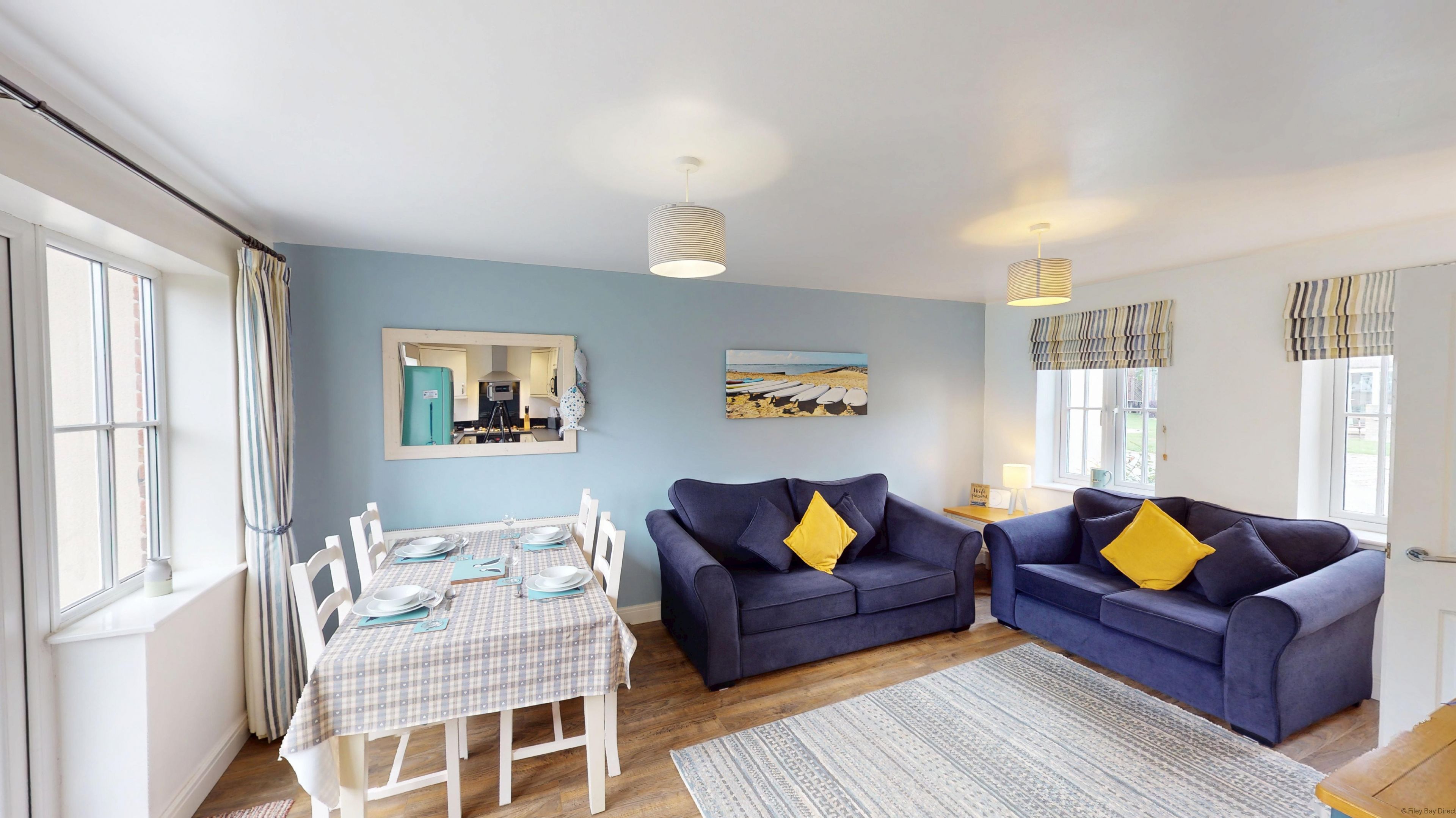 A living room with a blue sofa set, a dining table with plates, and a painting on the wall.