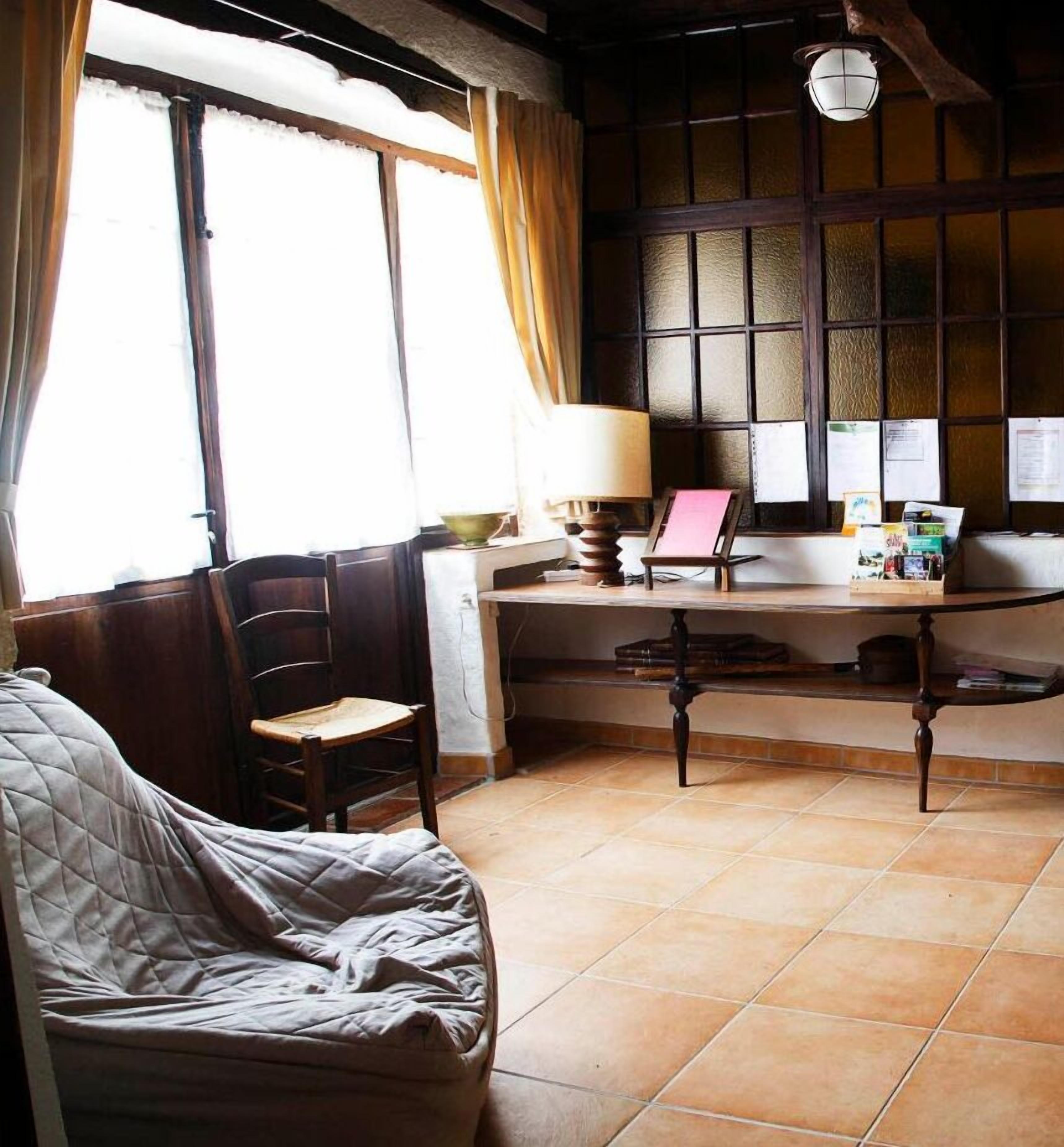 A cozy room with a bed, a desk, and a chair. There is a window with curtains, a lamp, and papers on the wall.