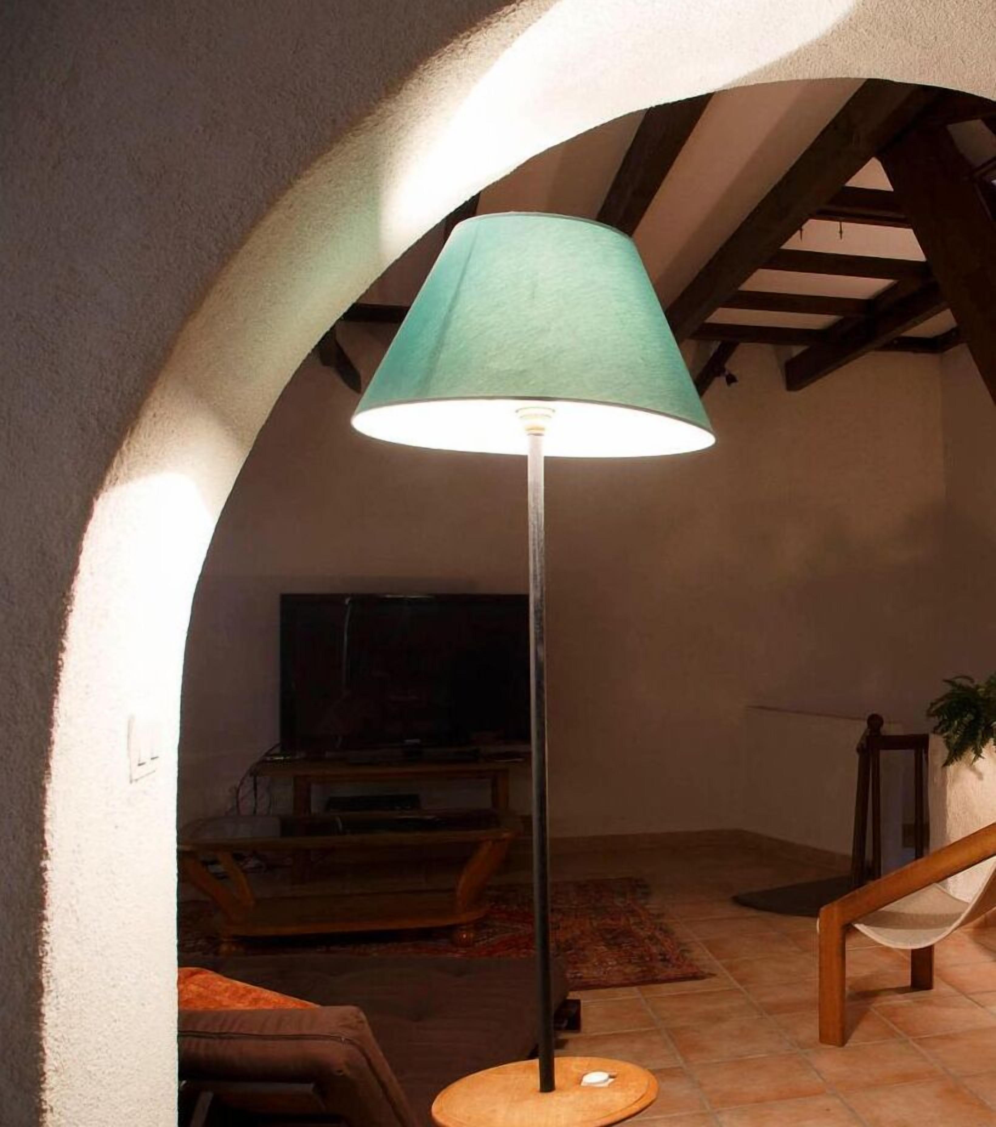 A floor lamp with a green shade in a room with a vaulted ceiling and exposed beams.