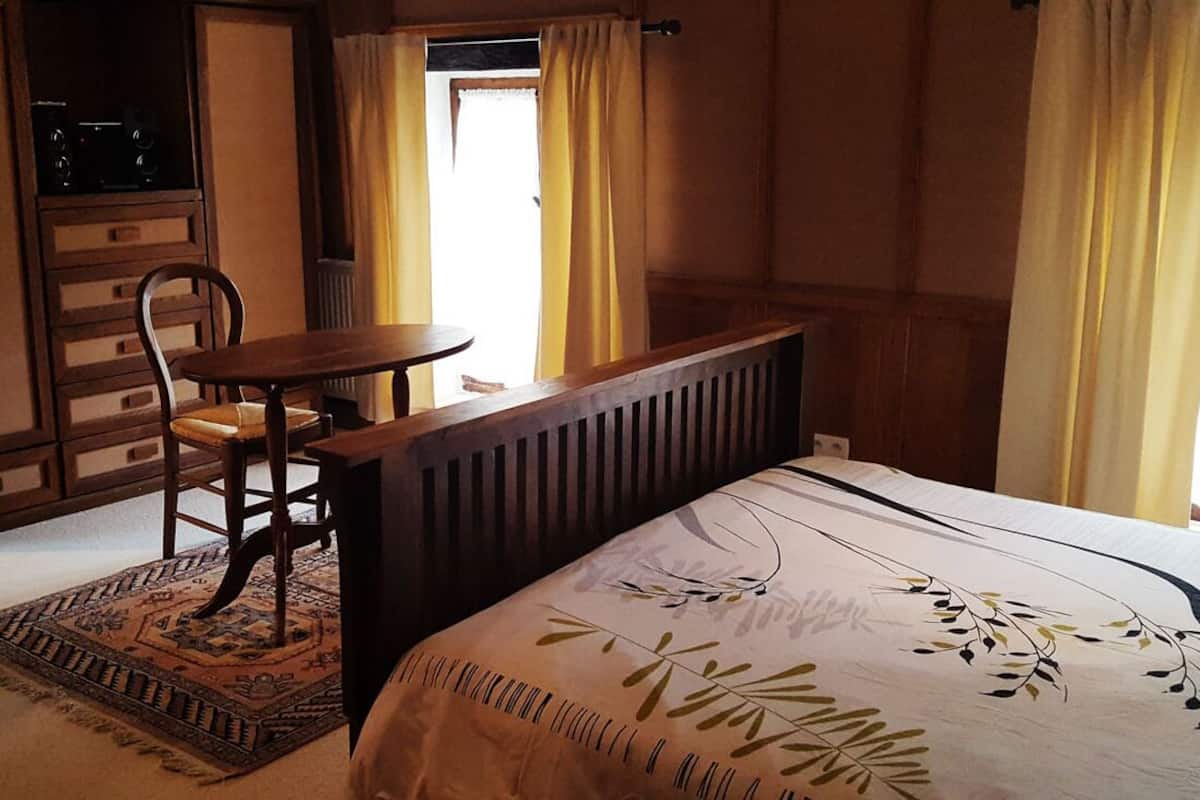 A bedroom with a bed, a wooden chair, a small table, and a radiator.
