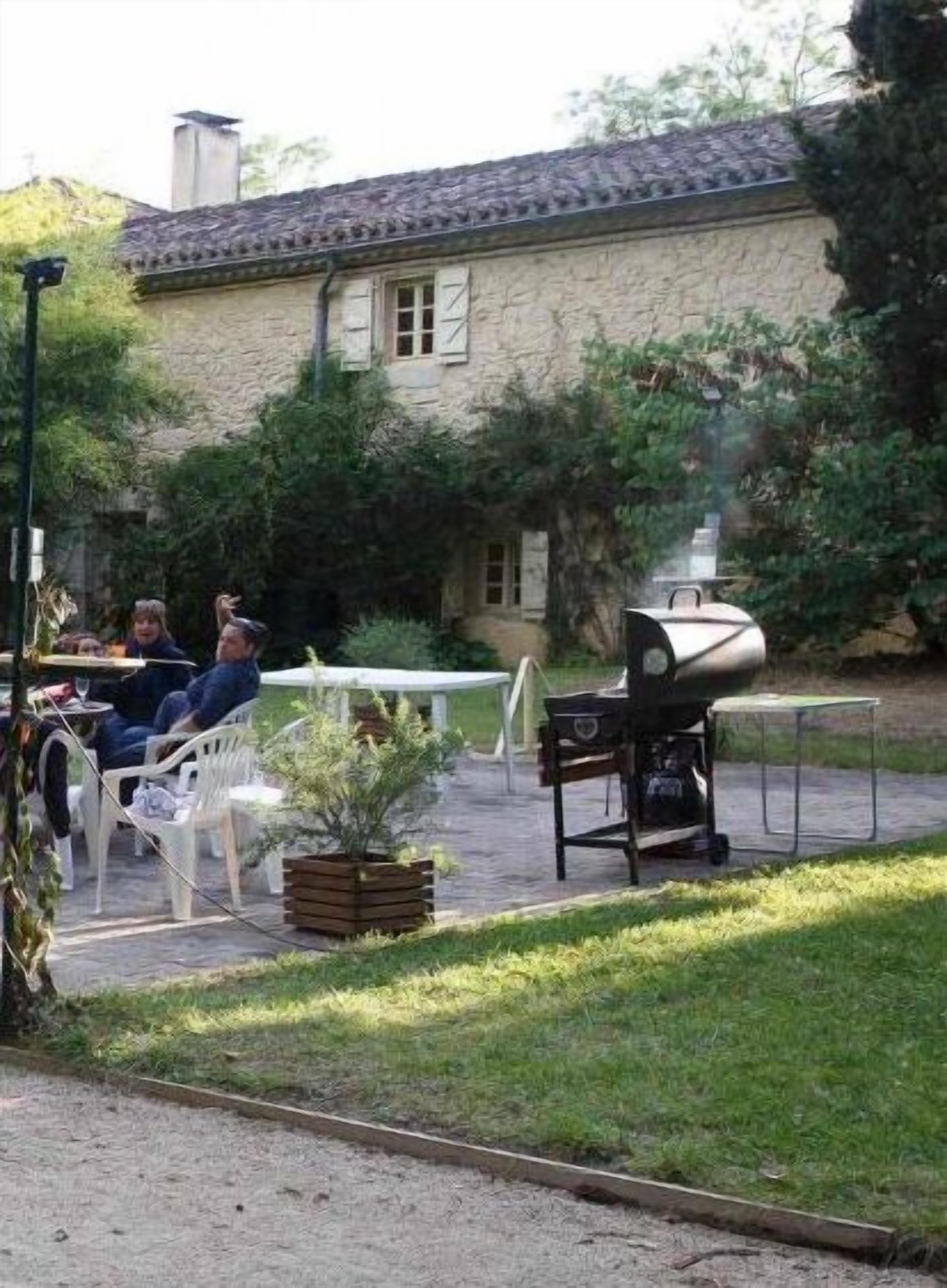 An outdoor patio area with stone walls, a barbecue grill, and a table with chairs.