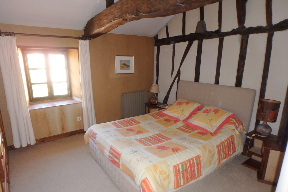 A bedroom with a large bed, a window with curtains, a nightstand, and a picture on the wall.