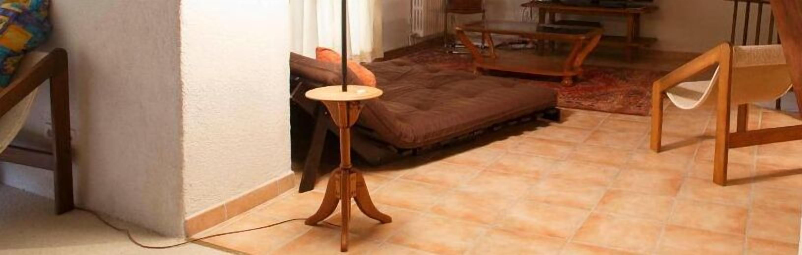 A room with a brown sofa, a wooden chair, a small round table, and a lamp on a tripod stand.
