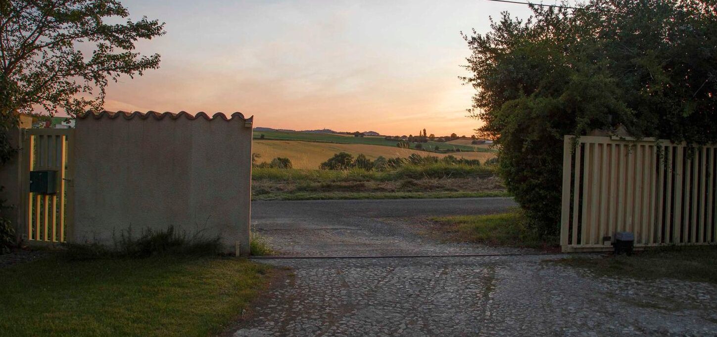 A rural road leading to a gated area with a small shed and a fence.