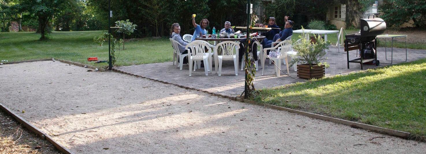 An outdoor patio with a dining table and chairs, a barbecue grill, and a croquet field.
