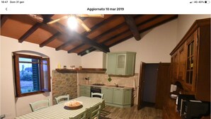 A rustic kitchen with a stone wall, wooden cabinets, and a checkered tablecloth. - Holiday home in the Florentine Chianti area (Reggello)