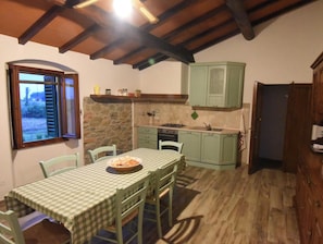 A rustic kitchen with a stone wall, a wooden ceiling, and a dining table with chairs. - Holiday home in the Florentine Chianti area (Reggello)