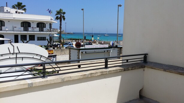 Un balcón con vista al mar, un edificio con un letrero que dice 'Food and Drink', y coches estacionados.