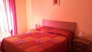 Un dormitorio con cama, mesita de noche, lámpara y un cuadro en la pared.