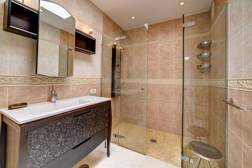 A modern bathroom with a glass-enclosed shower, a vanity with a mirror, and decorative wall tiles.
