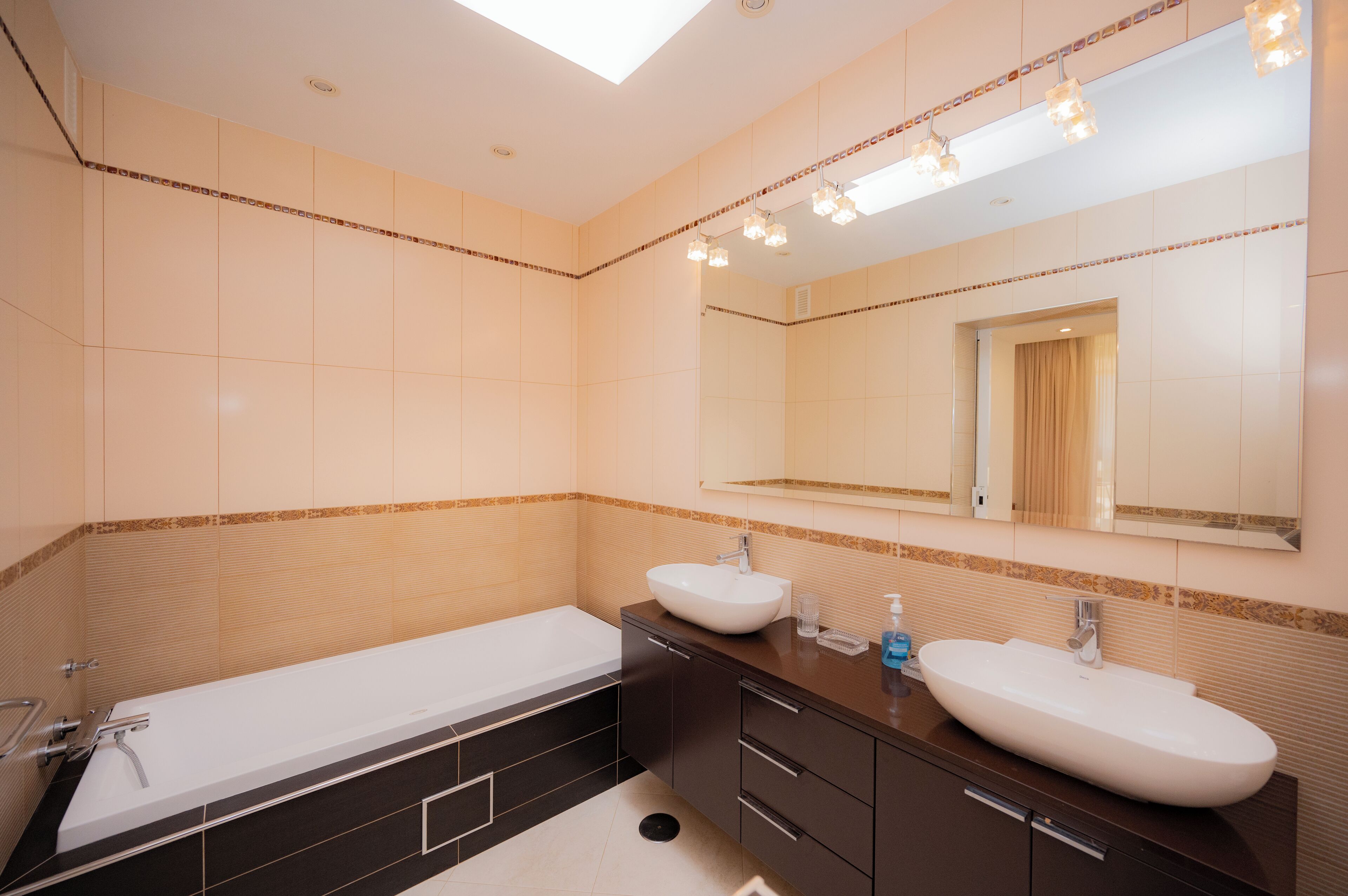 A modern bathroom with a large bathtub, two sinks, and a large mirror.
