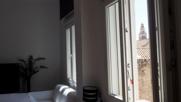 Ein Schlafzimmer mit einem Bett, einem Nachttisch, einer Lampe und einem Fenster mit Blick auf ein Gebäude.