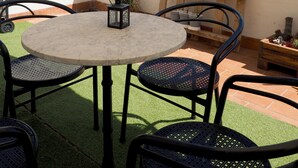 Eine Terrasse mit einem runden Tisch und Stühlen, umgeben von Kübelpflanzen und einem hölzernen Pflanzkasten.