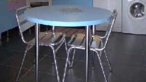 A compact kitchen with a round table, chairs, a washing machine, and a coffee maker.