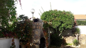 Un horno de piedra al aire libre con chimenea, rodeado de abundante vegetación y un muro de ladrillo.