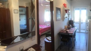 Una habitación de hotel con una cama, un escritorio, una silla, una mesita, un espejo, un armario y una puerta que da a un balcón.