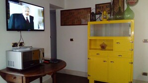 A room with a television displaying a program, a yellow cabinet, and a wooden table. - APARTMENT IN THE HISTORICAL CENTER OF CATANIA (CATANIA)