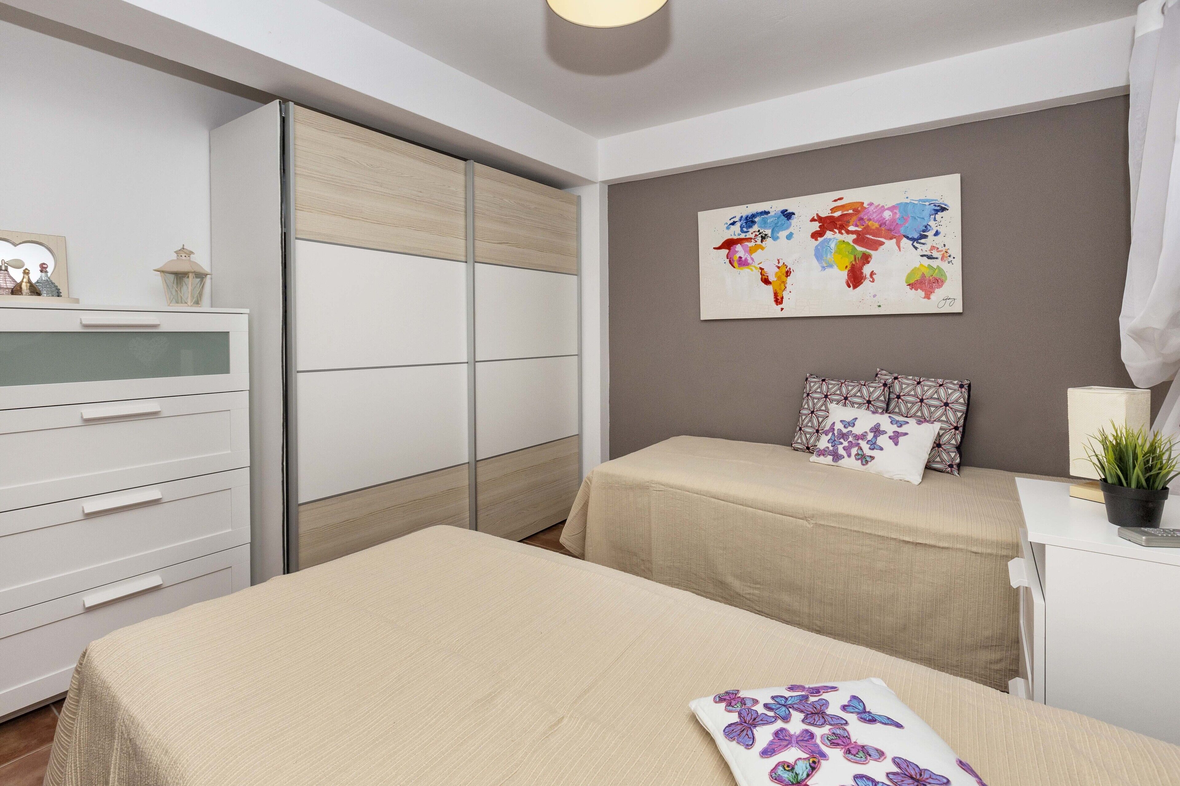 A modern bedroom with two beds, a wardrobe, a desk, and a world map artwork.