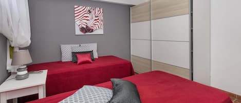 Ein Schlafzimmer mit zwei Betten, einem Nachttisch mit Lampe, einem Wandbild mit Zebra-Motiv und einem Kleiderschrank mit Schiebetüren.