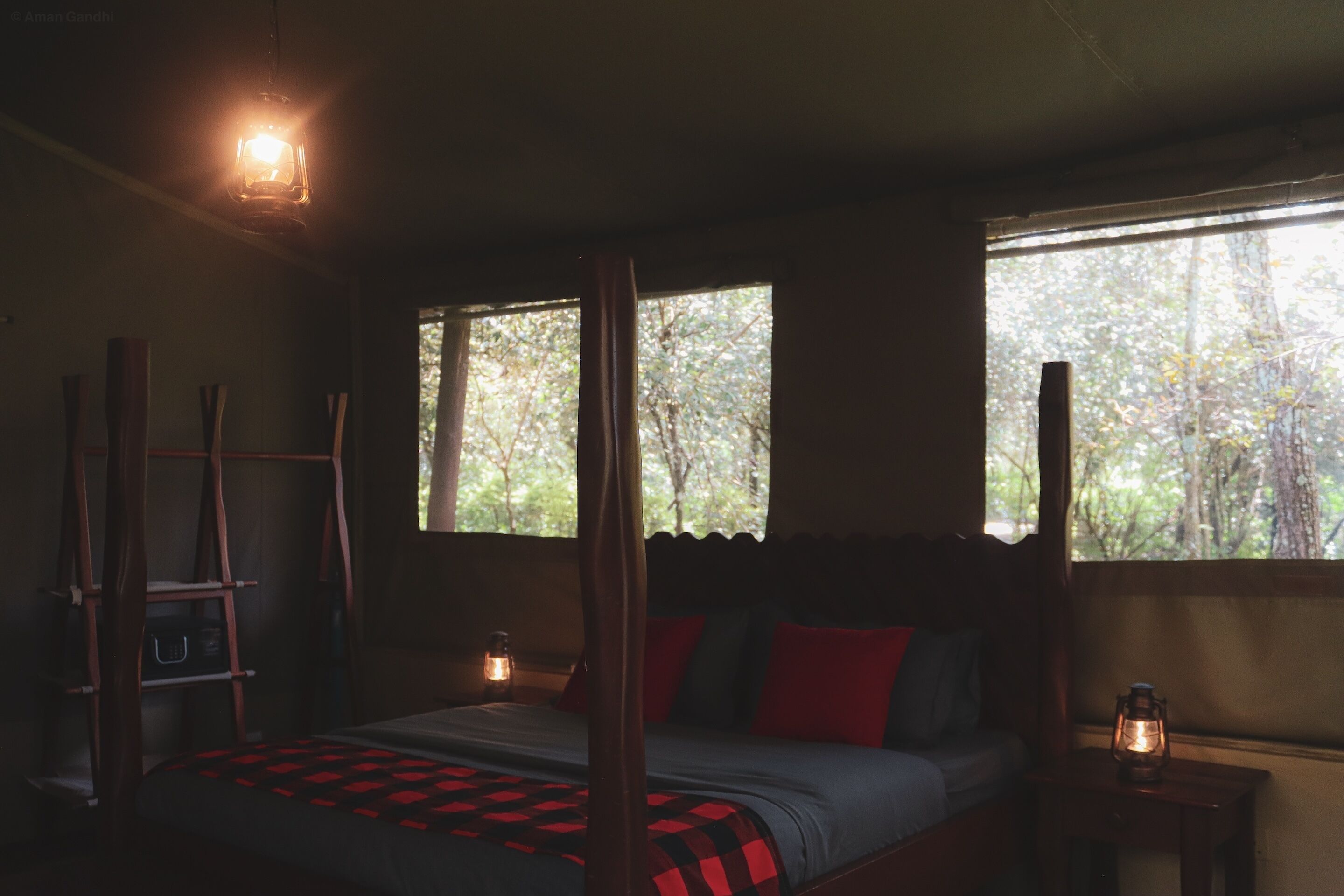A dimly lit room with a bed, a wooden ladder, and a window with a view of trees.
