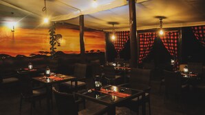 Un comedor interior con mesas y sillas, un techo con luces colgantes y un mural en la pared.