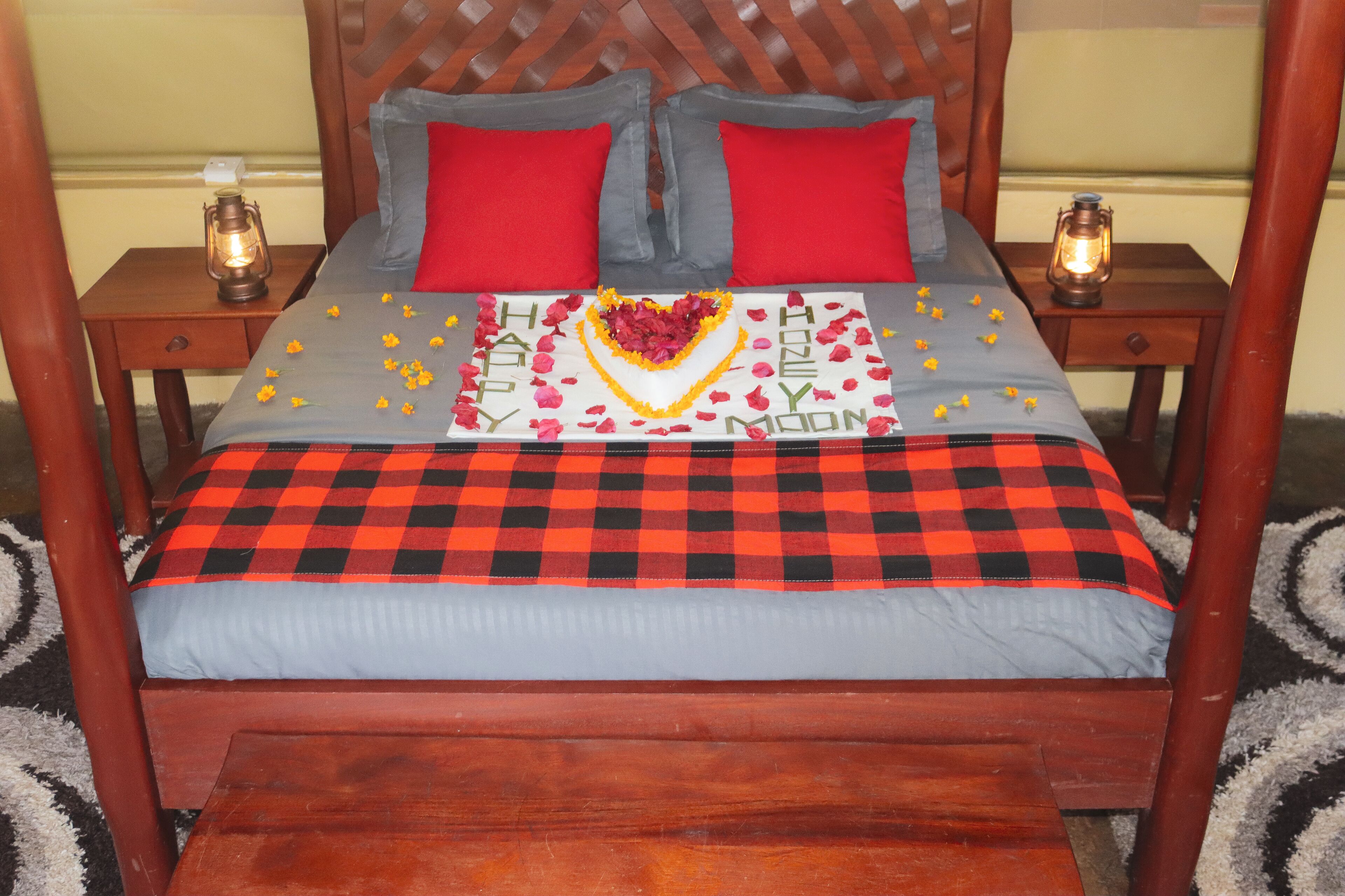 A bed with a checkered bedspread, red and grey pillows, and a heart-shaped decoration with 'Happy New Year' written on it.