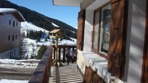 A balcony with a wooden railing overlooking a snowy landscape and a mountain.