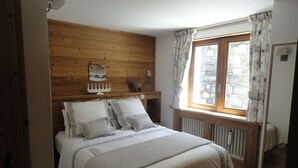 A bedroom with a wooden headboard, a bed with white bedding, a stone wall, and a window with curtains.