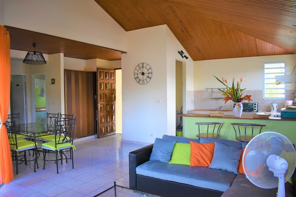 Uma sala de estar com um sofá, cadeiras, um ventilador e um relógio na parede.