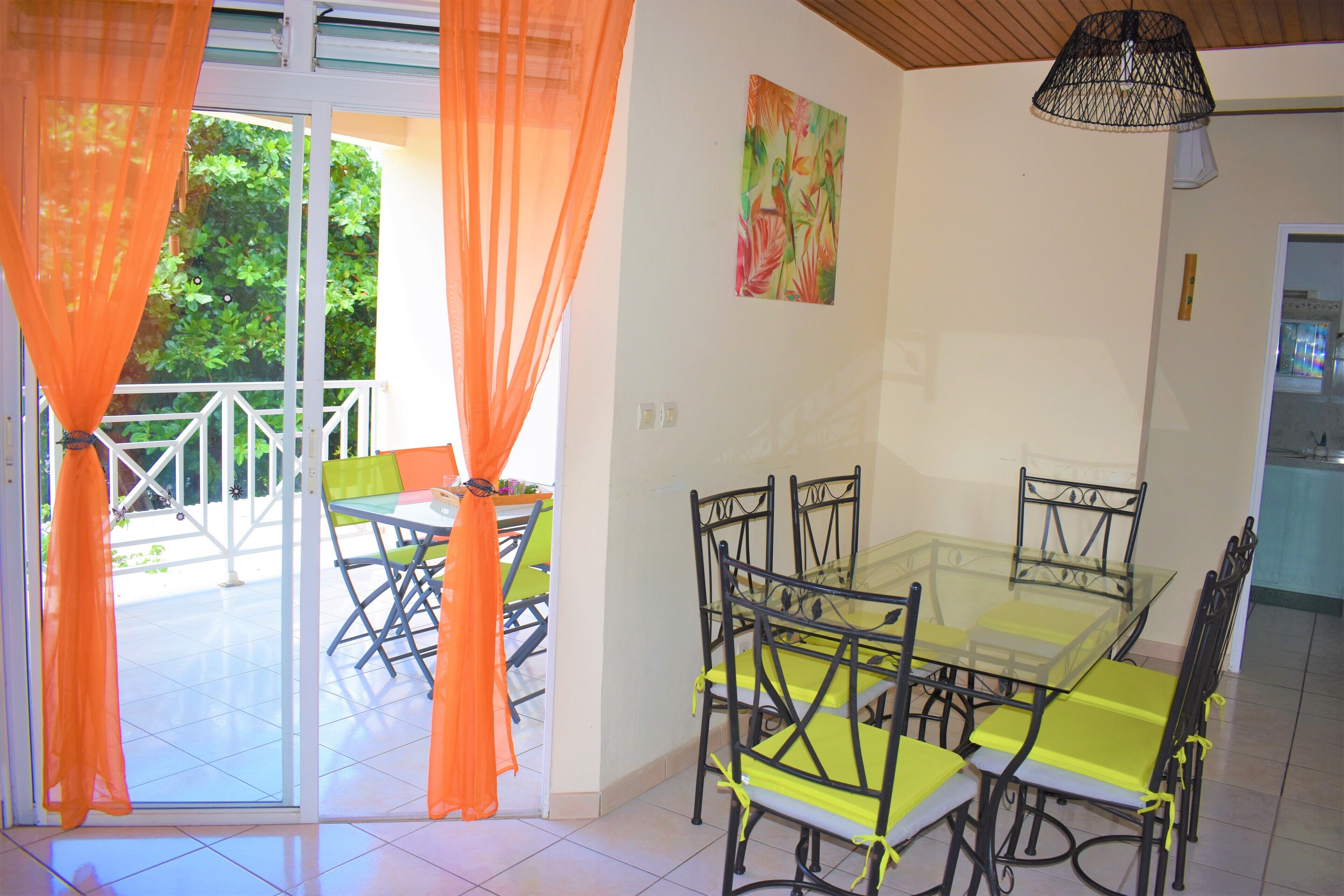 Un coin repas avec une table et des chaises en verre, des rideaux orange et un tableau accroché au mur.
